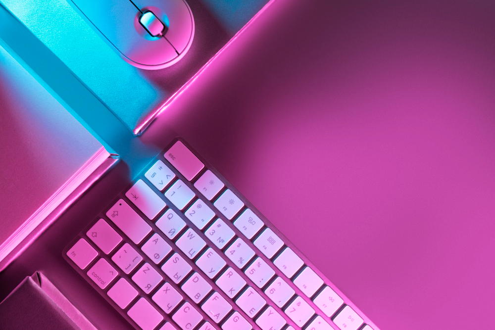 Teclado e mouse iluminados com luzes neon rosa e azul sobre mesa de trabalho moderna