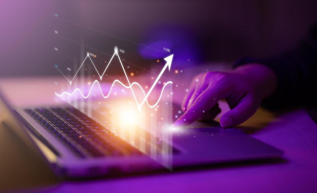Gráfico digital holográfico sobre laptop com mão apontando, representando análise de dados, crescimento e inovação tecnológica.
